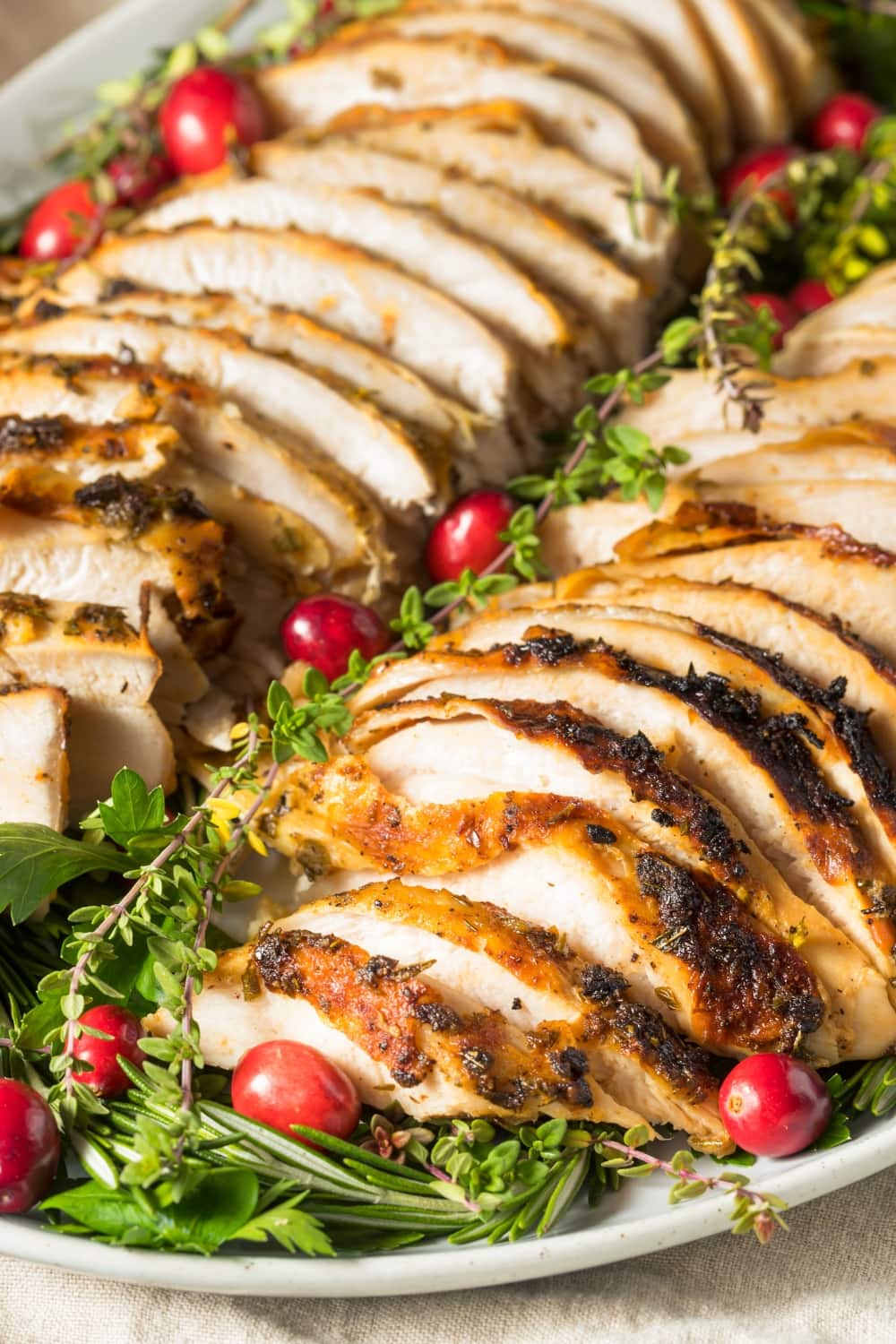 Sliced turkey breast with cranberries and herbs served on a white huge plate.