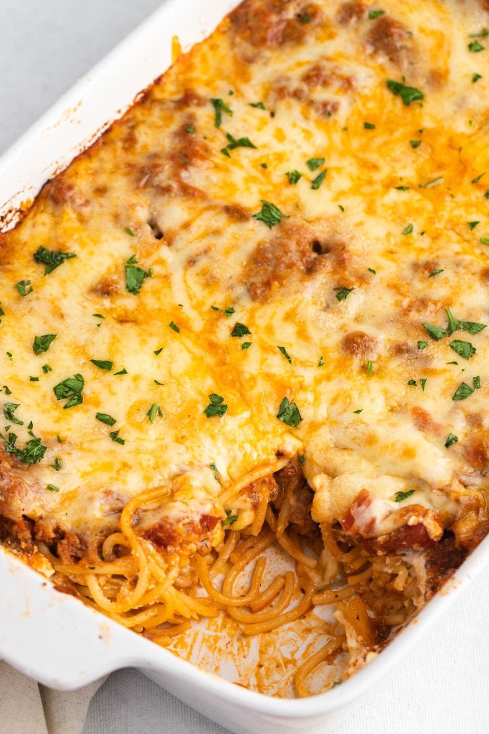 Portion Sliced Homemade Million Dollar Spaghetti with Cheese and Herbs on a White Baking Dish