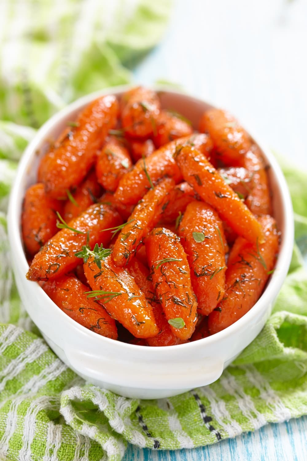 Honey glazed baby carrots with herbs in a small white bowl. 