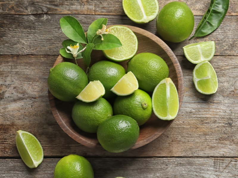 Whole and Slice Lime on a Wooden Bowl