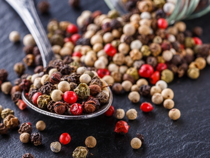 Mixed Peppercorns on a Spoon on a Dark Stone Background