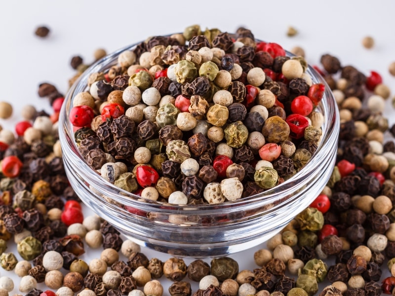 Black, green, white and red peppercorns on a glass spice bowl