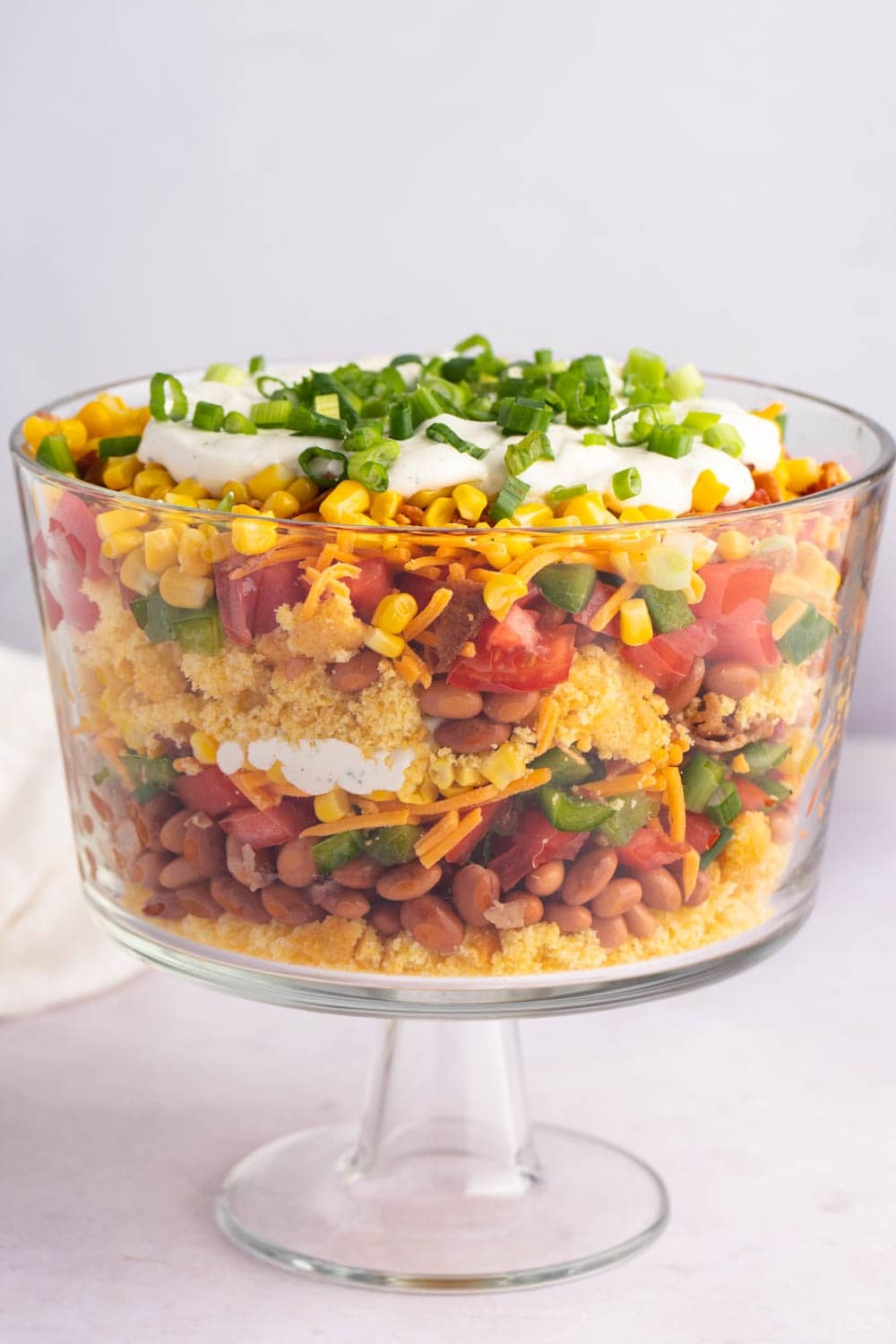 Layered Cornbread Salad with Tomatoes, Bell Peppers, Beans, Onions, Cheese and Bacon, Served on a Huge Glass Bowl