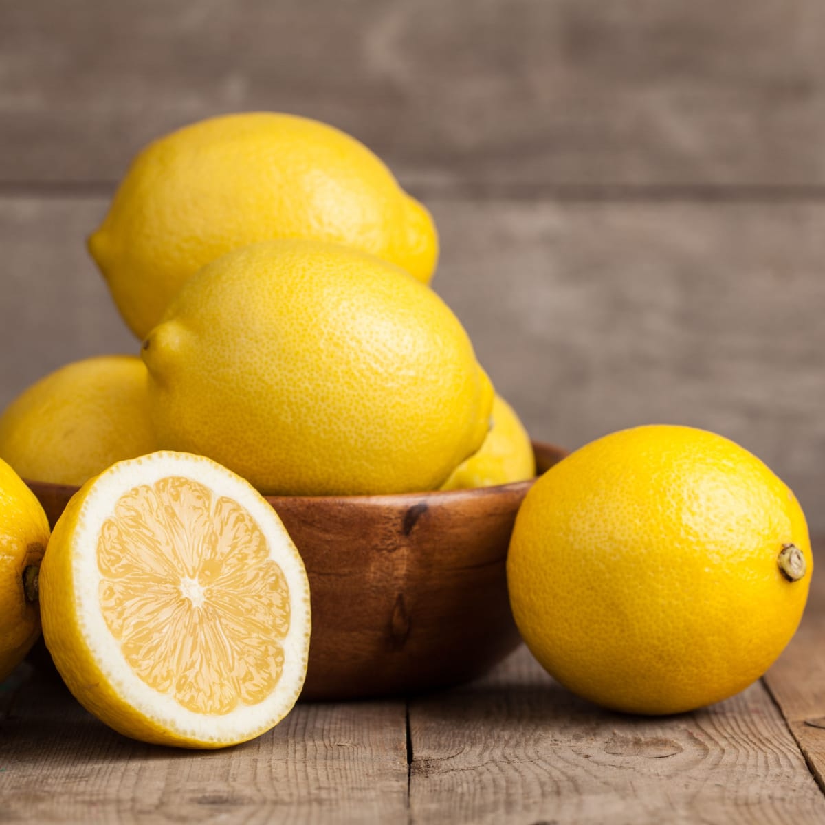 Ripe Lemons on a Wooden Bowl Placed on Top of a Dark Brown Wooden Table

