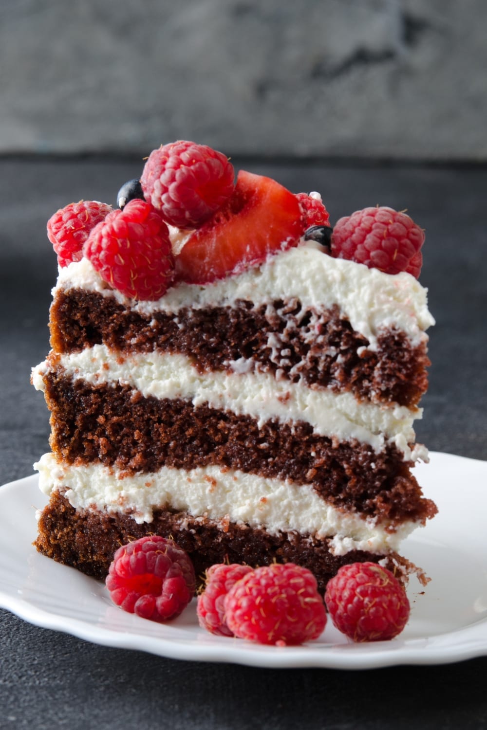 Sliced Layered Naked Chocolate Cake with Cream and Raspberries, Served on a White Plate