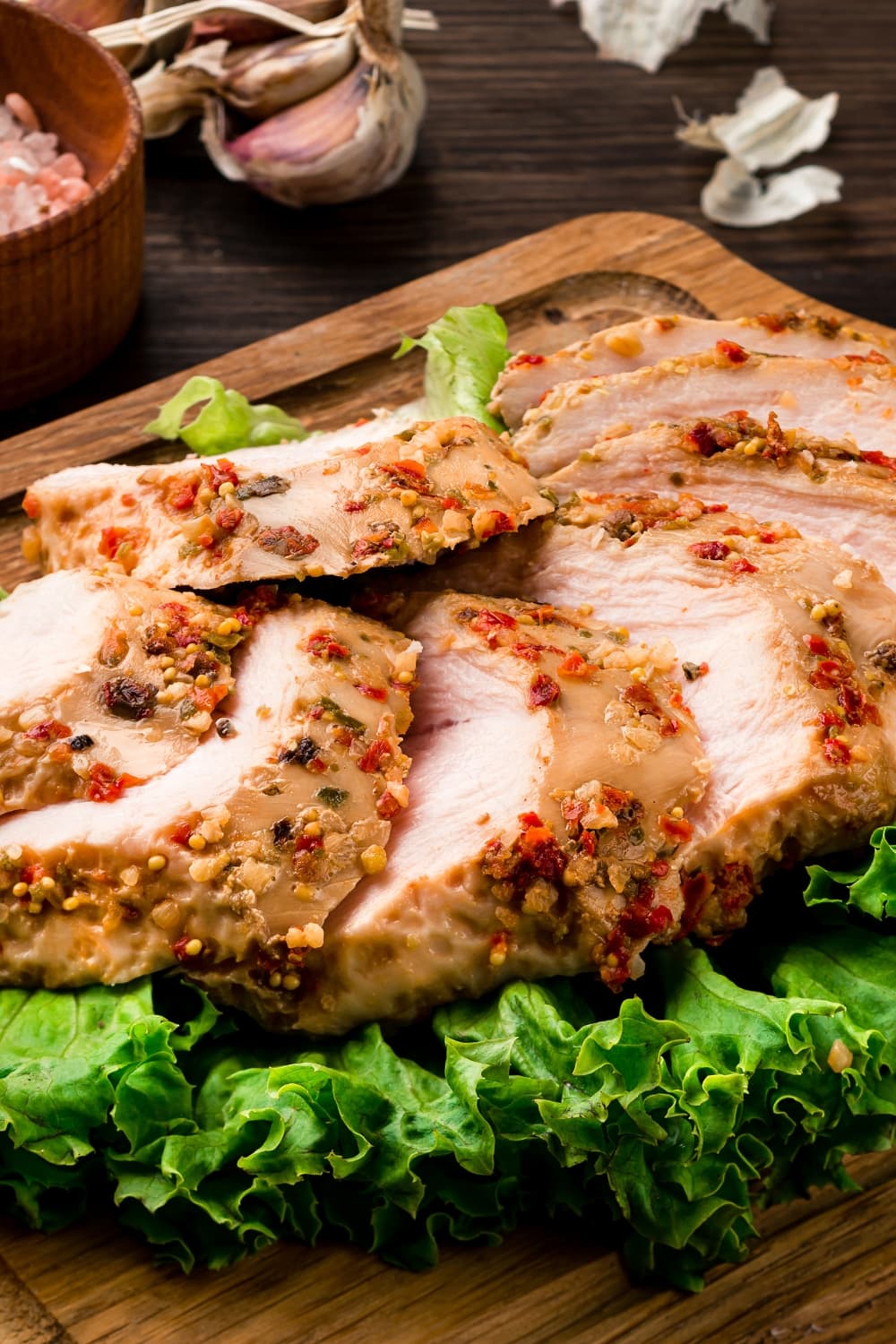 Sliced Sous Vide Chicken Breast with Green Lettuce Leaves Plated on a Wooden Cutting Board