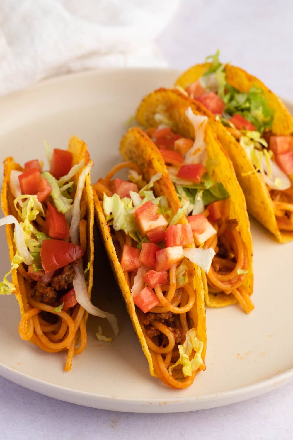 Spaghetti Tacos Loaded with Onions, Tomatoes, Lettuce and Ground Meat Served on a Plate