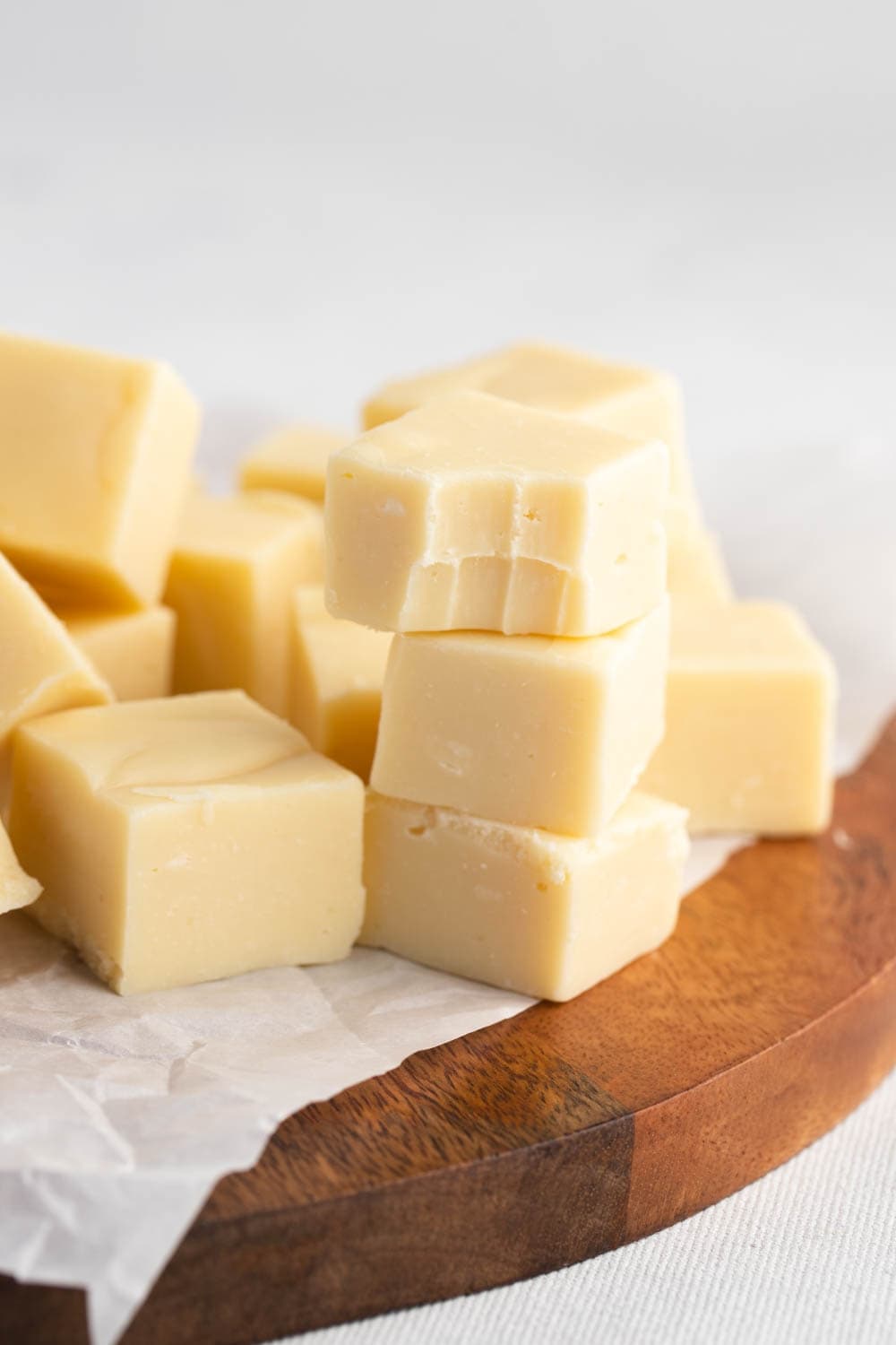 A stack of cube cut white chocolate fudge, on top of a parchment paper on a round wooden board