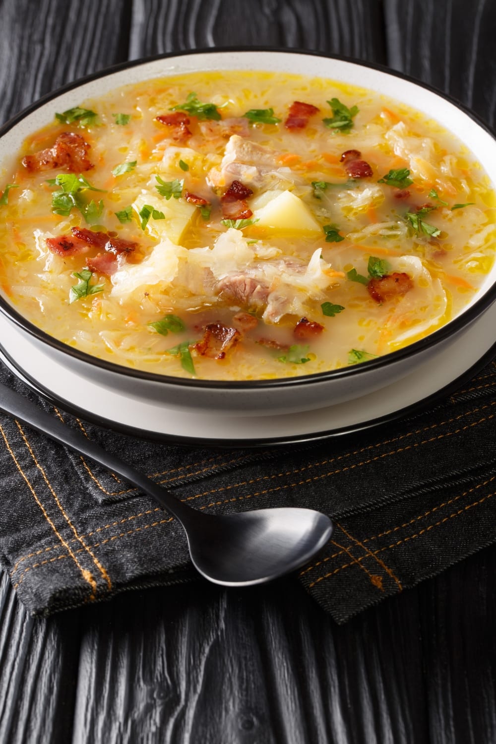 A Bowl of Polish Potato and Cabbage Soup with Bacon Bits and Chicken Meat, Garnished With Chopped Parsley Leaves