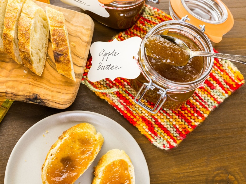 Apple butter and bread slices arranged on top of wooden table. 