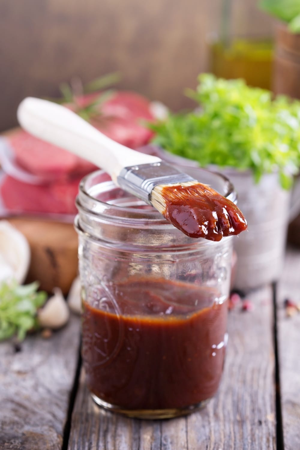 A brush with sauce placed on top of a glass jar half filled with homemade BBQ sauce. 