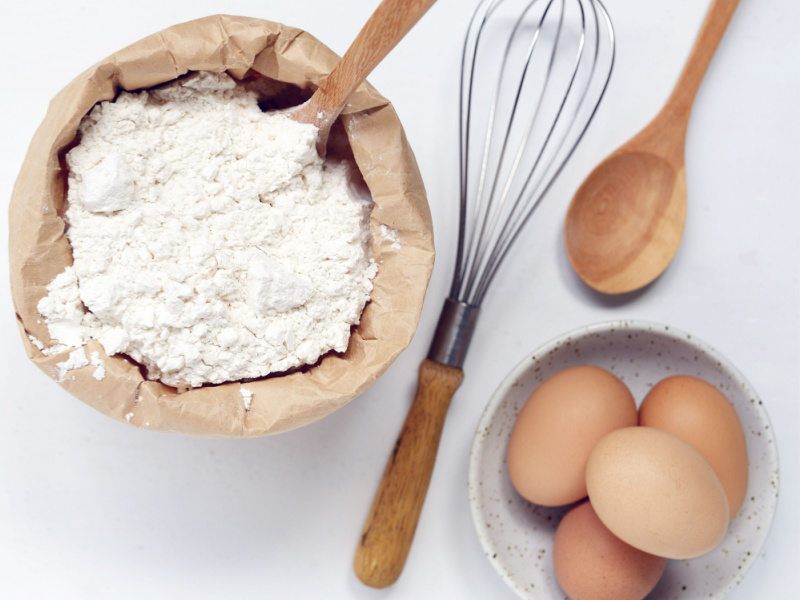 Whisk, Eggs, Wooden Spoon and Cake Flour on a Paper Sack 