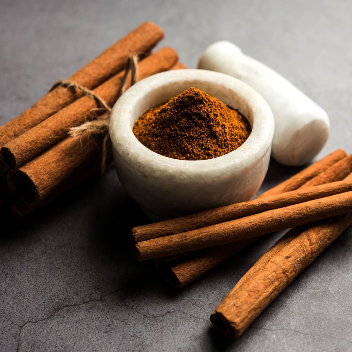 Cinnamon Stick Bundles Next to a Pestle and Mortar Filled With Powdered Cinnamon