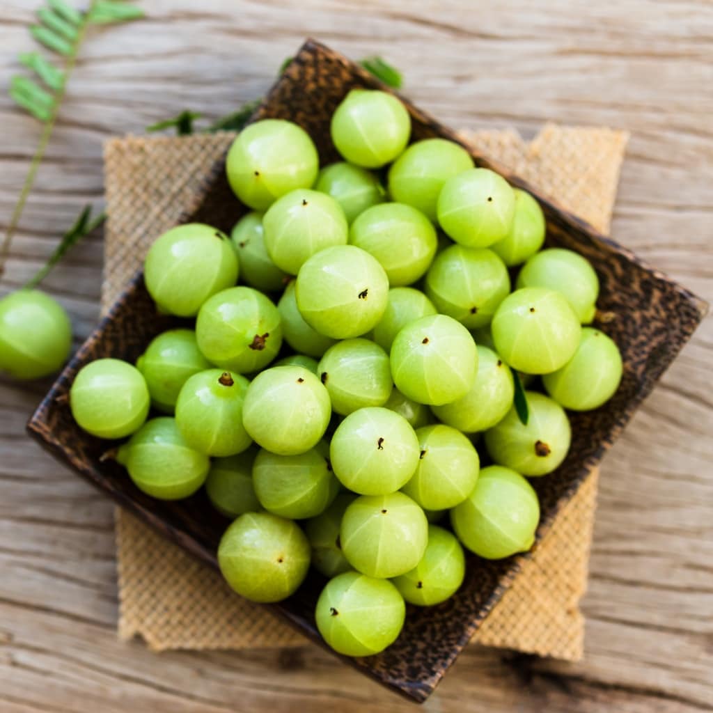 Top View of Bunch of Fresh Organic Green Gooseberries on a Wooden Square Bowl Placed on Top of a Woven Mat