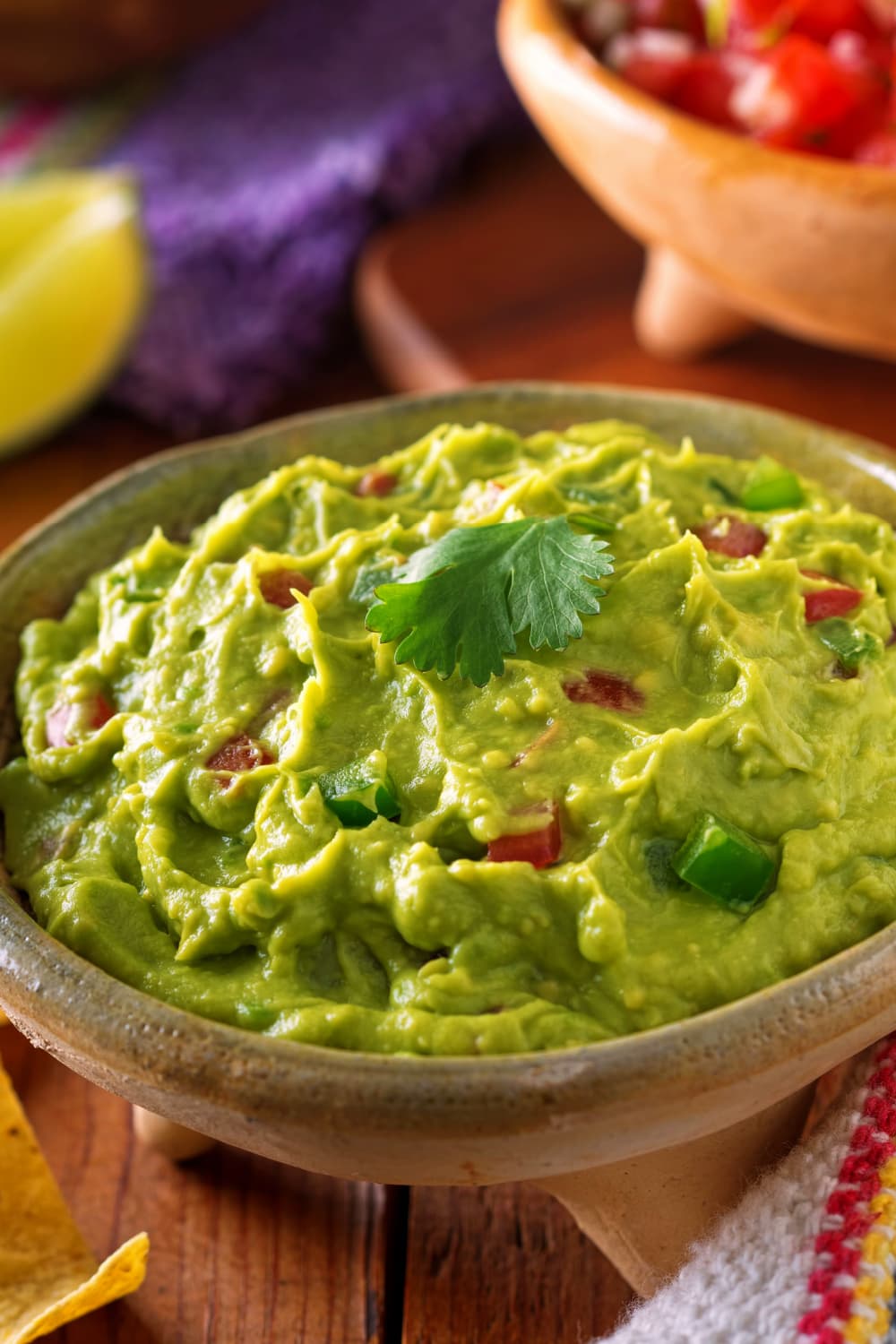 Creamy guacamole with slices of tomatoes served on a brown bowl. 