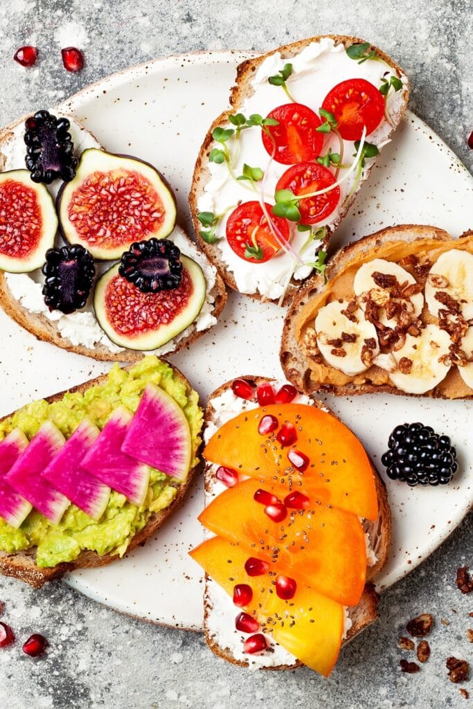 Healthy Breakfast Tartine with Watermelon, Peanut Butter, Banana, Chocolate Granola, Avocado, Persimmon, Tomatoes and Figs
