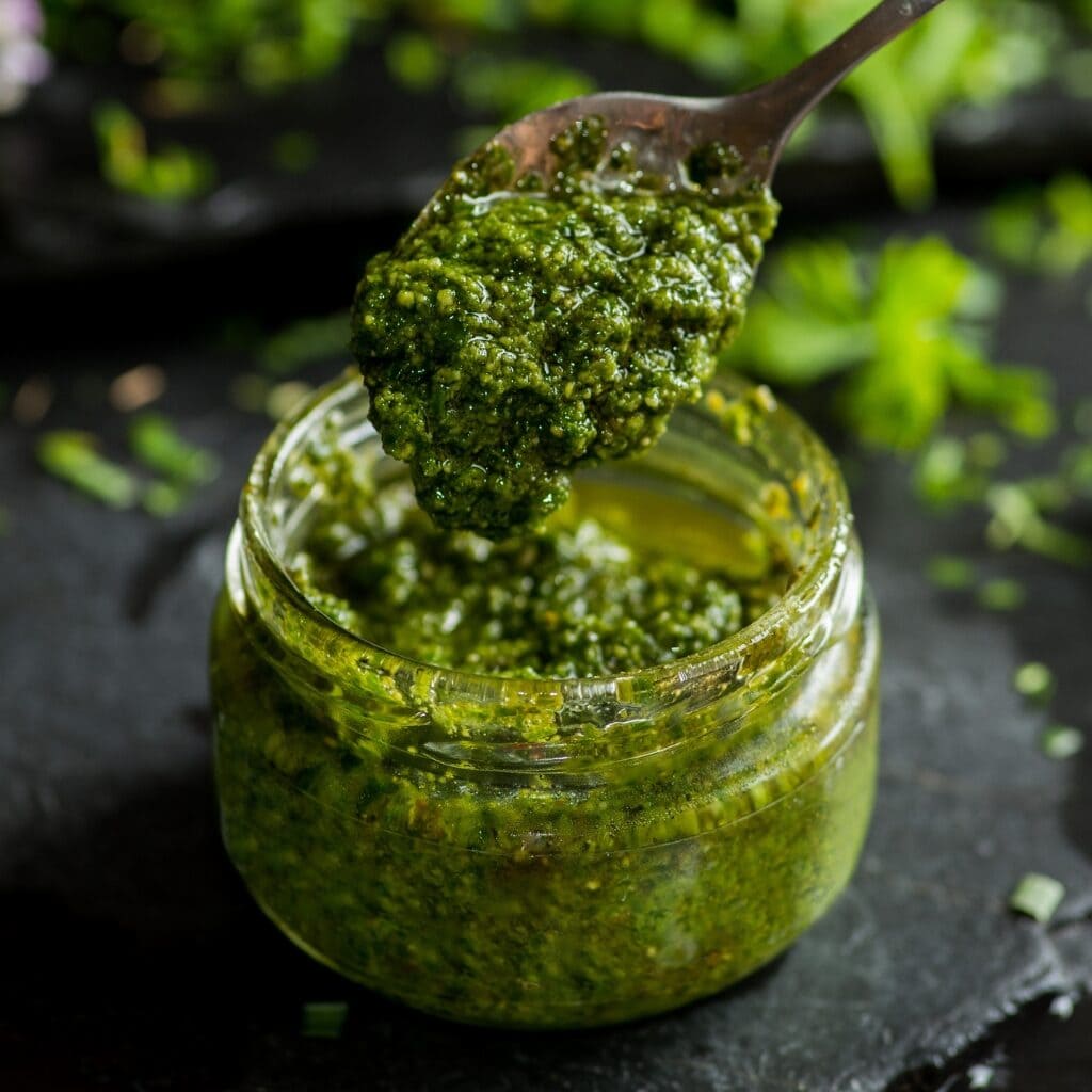 Spoon Scooping Green Pesto From a Small Glass Jar