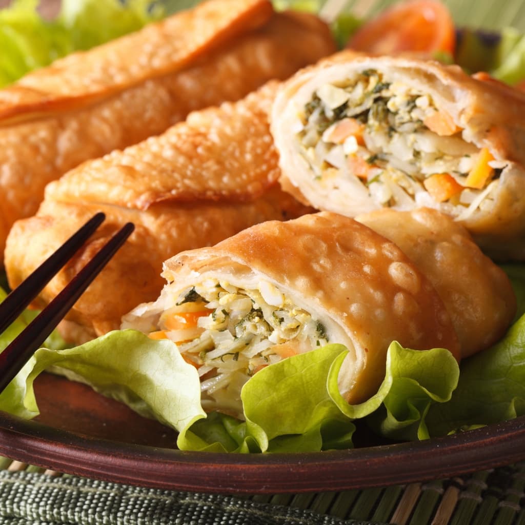 Fried spring rolls plated with bed of fresh lettuce served on a brown wooden plate with chopsticks. 