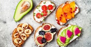 Healthy Breakfast Tartine with Watermelon, Peanut Butter, Banana, Chocolate Granola, Avocado, Persimmon, Tomatoes and Figs