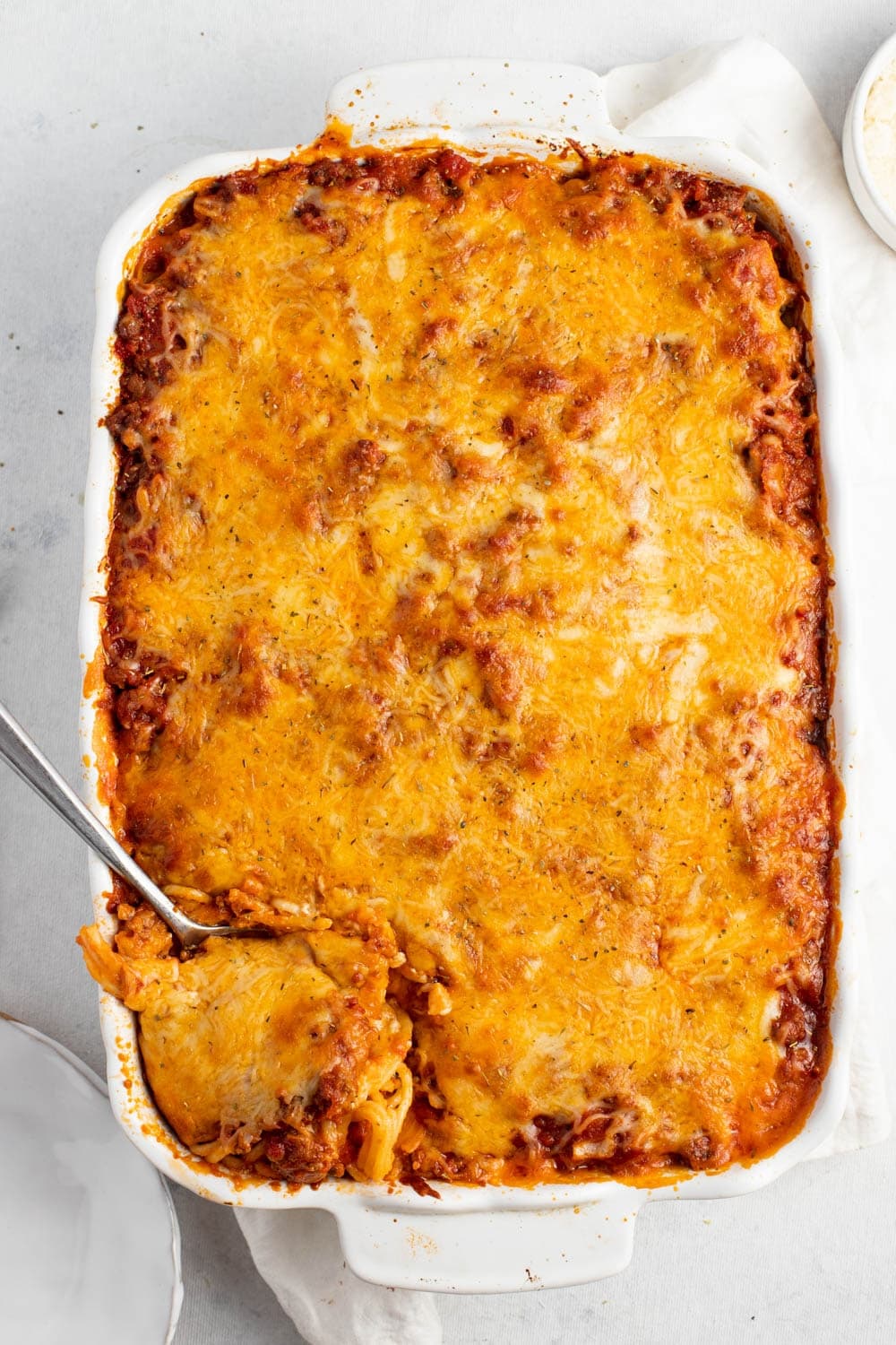 Top View of Baked Spaghetti in a white rectangular baking dish, with spoon dipped on it for serving. 