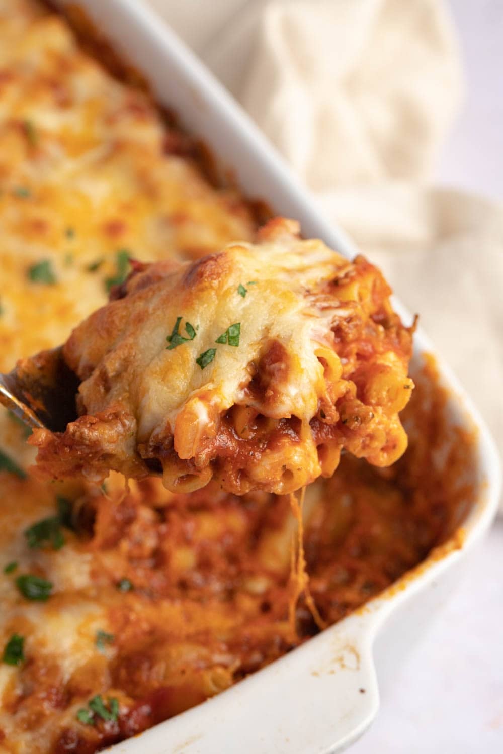 Spoonful of baked ziti from a casserole dish. 