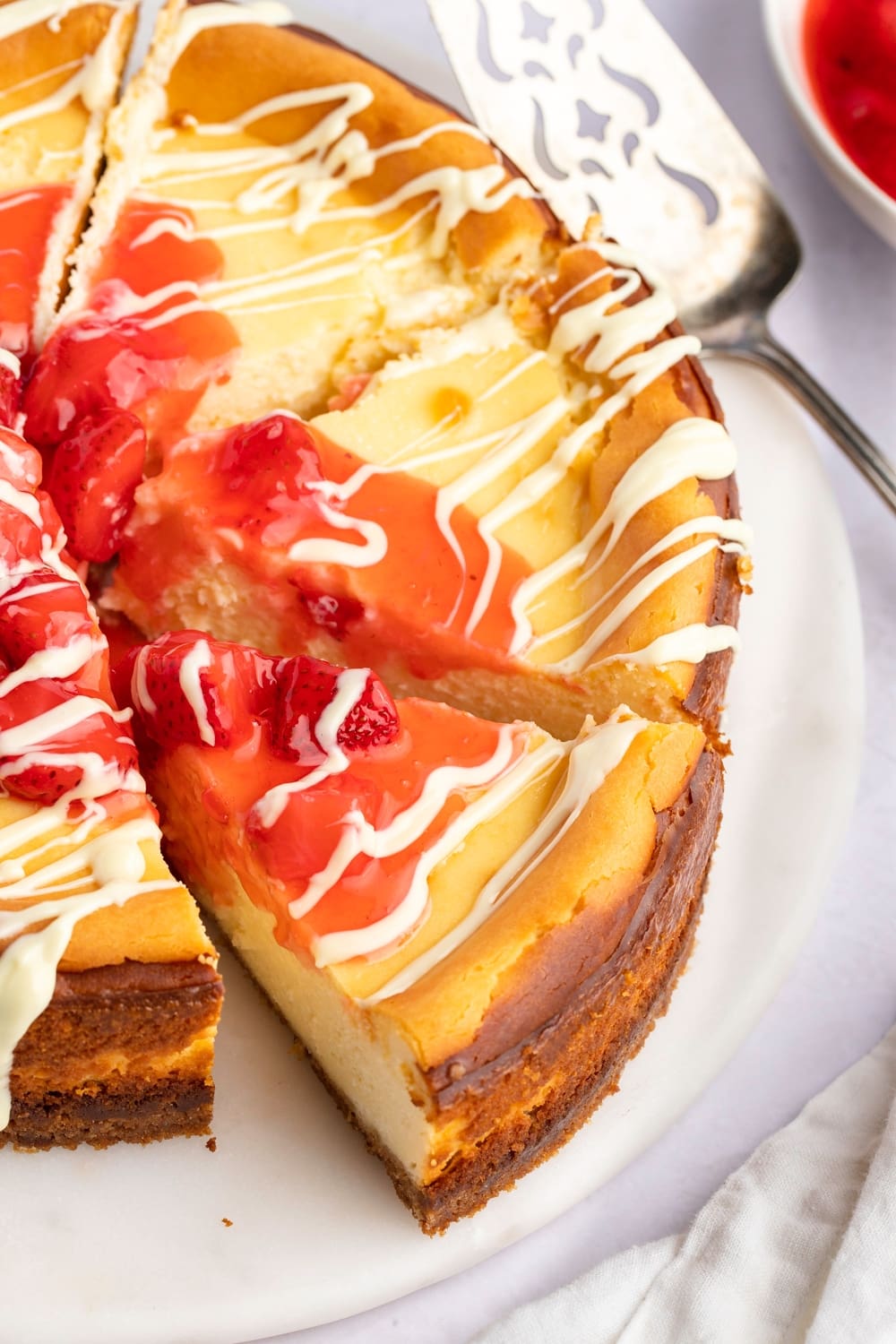 Sliced Whole White Chocolate Cheesecake with Strawberry Sauce Drizzled With White Syrup