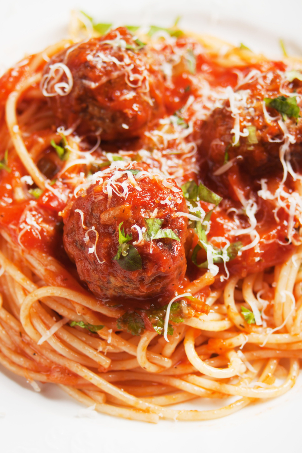 Spaghetti pasta topped with meatballs topped parmesan cheese. 