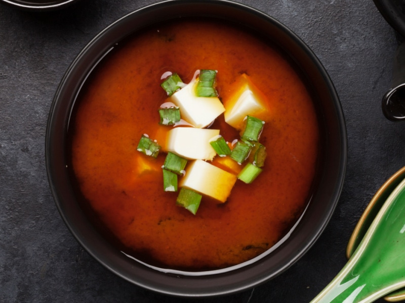 Red soup on a black bowl with tofu and sliced green onions
