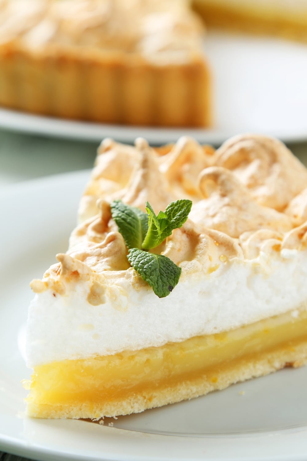 A Sliced of Layered No-Bake Lemon Pie with Meringue Served on a White Plate, Garnished With Fresh  Basil Leaves
