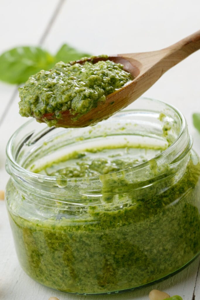 Homemade Ina Garten Pesto Sauce Scooped with a Wooden Spoon From a Small Glass Jar