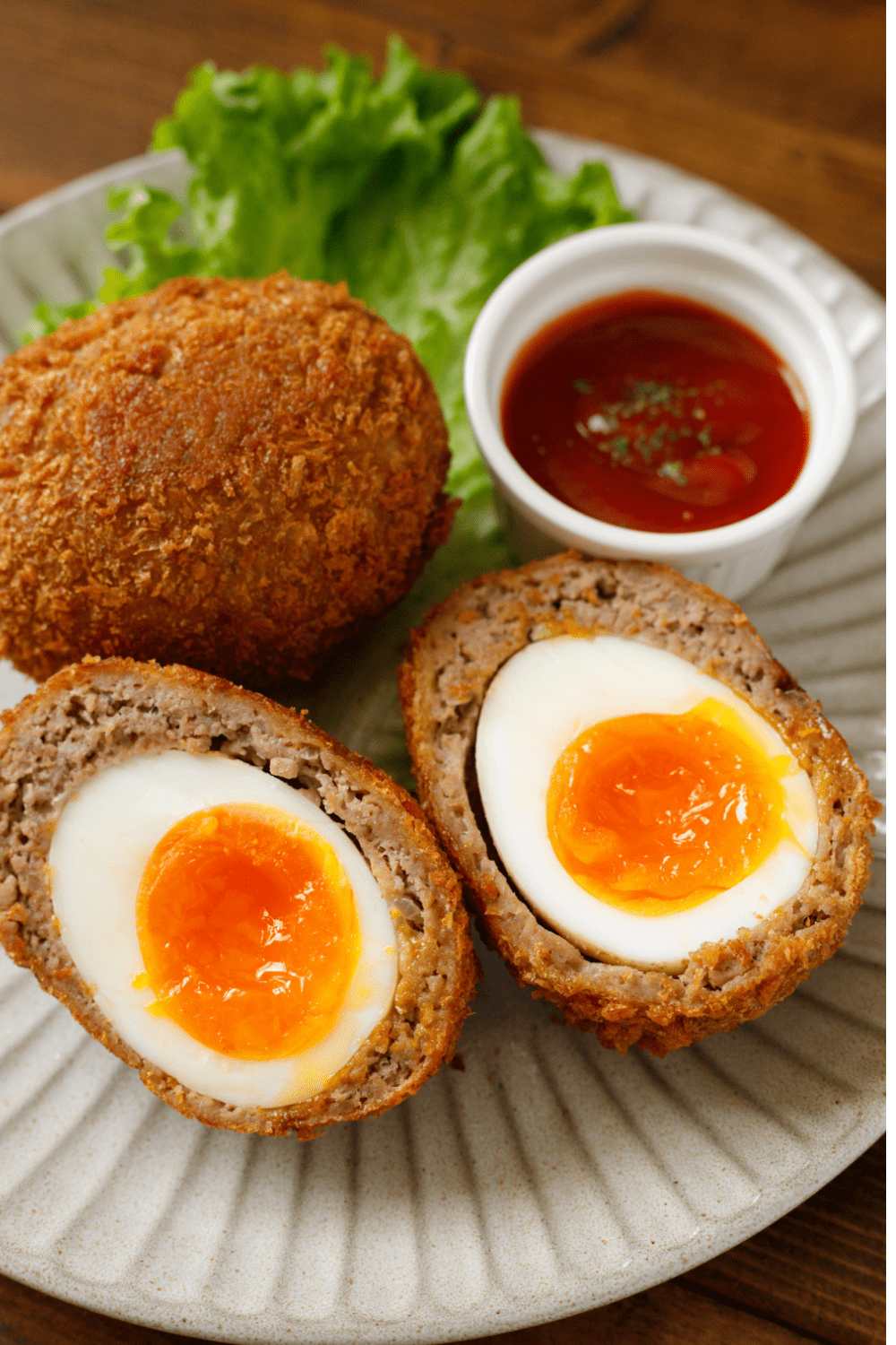 Whole and sliced in half Scotch Eggs on Plate served with red dipping sauce. 