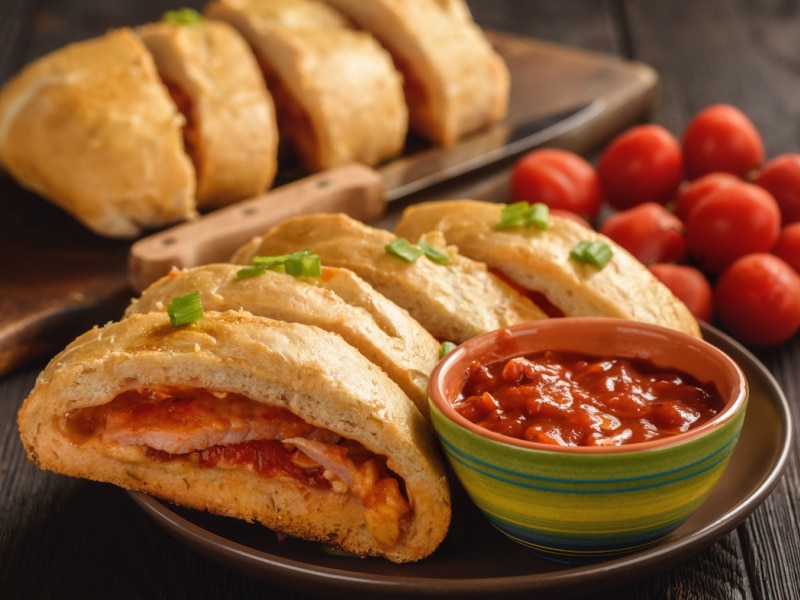 Crusty Stromboli Sliced with Extra Marinara Sauce Served on a Brown Plate 