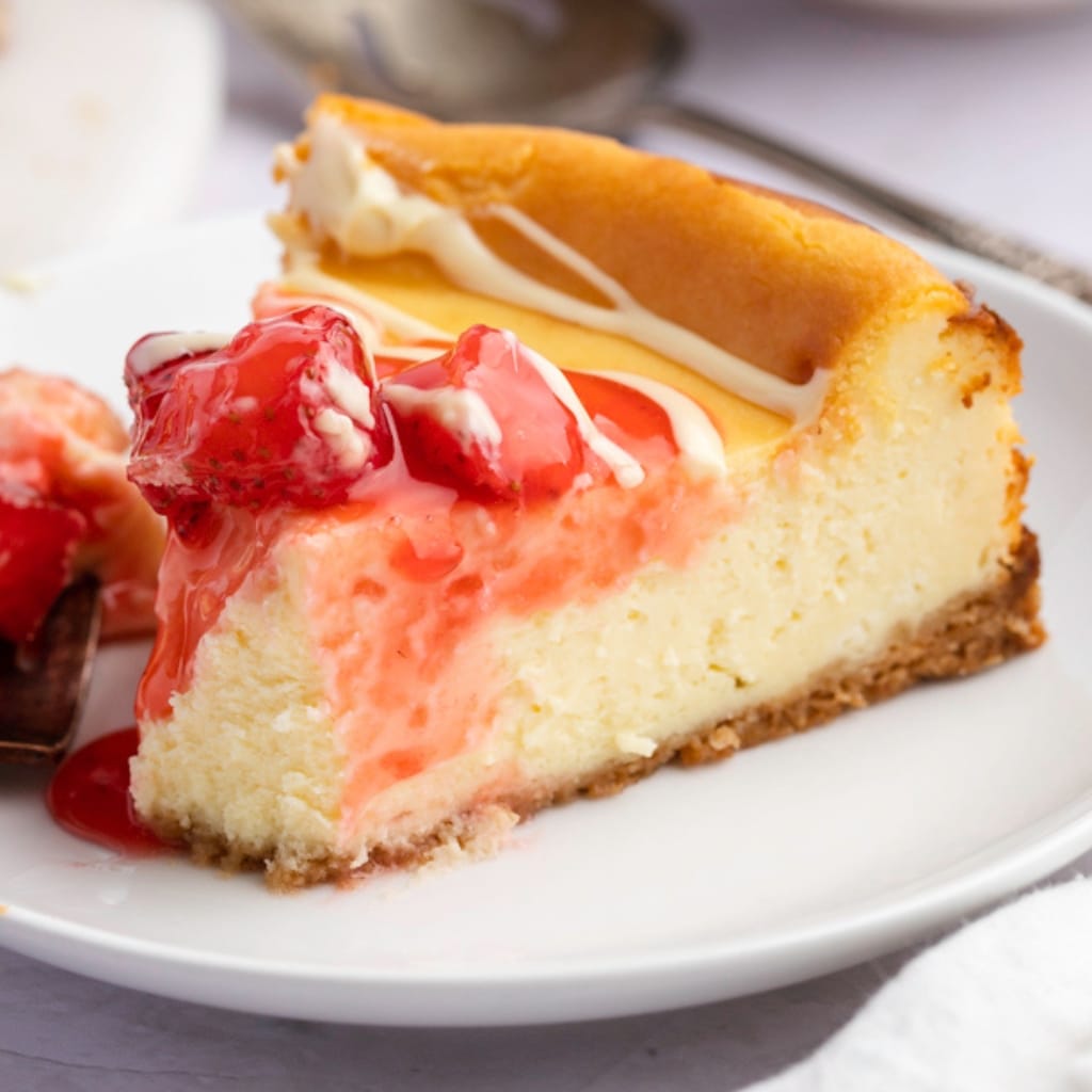 Close up of a Slice of White Chocolate Cheesecake with Strawberry Sauce in a White Plate