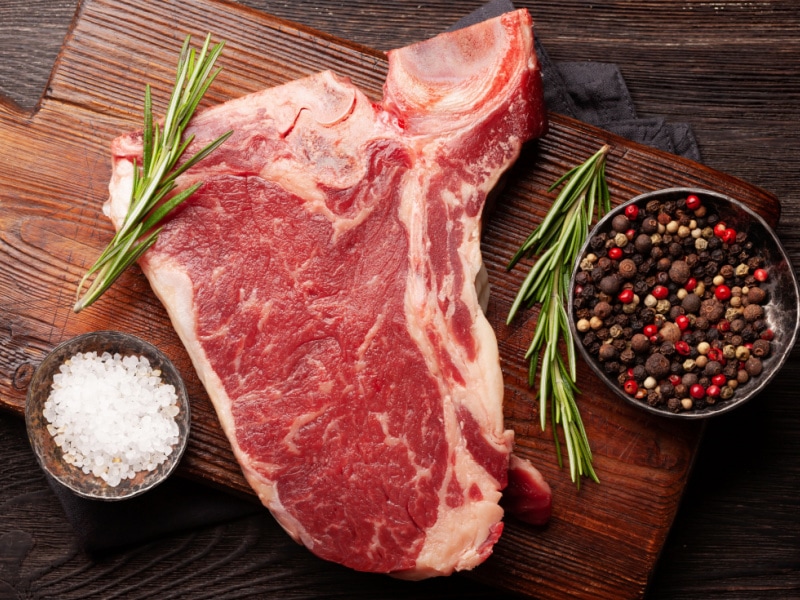 Raw T-bone Steak with Herbs and Spices on a Wooden Cutting Board