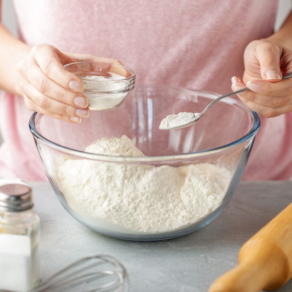Woman Adding Baking Powder in a Glass Bowl