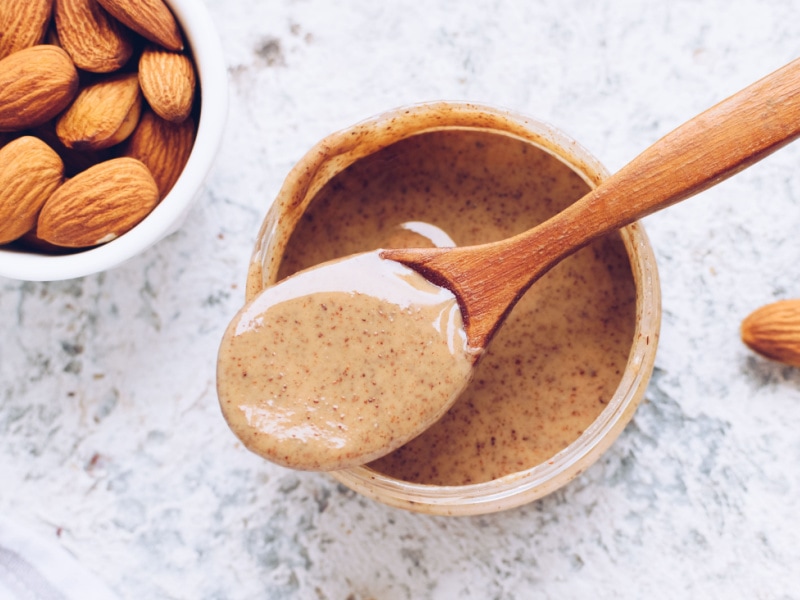 Creamy Almond Butter in a Bottle Scooped With a Wooden Spoon