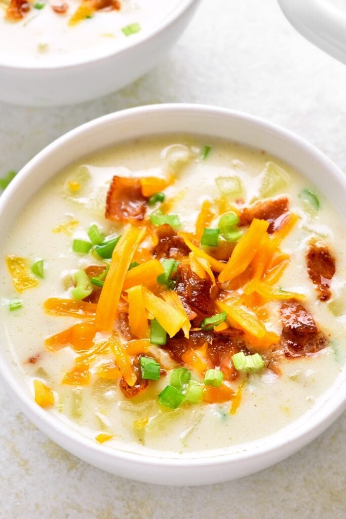 Bowl of Creamy Potato Soup With Cheese, Bacon and Sliced Greens on Top