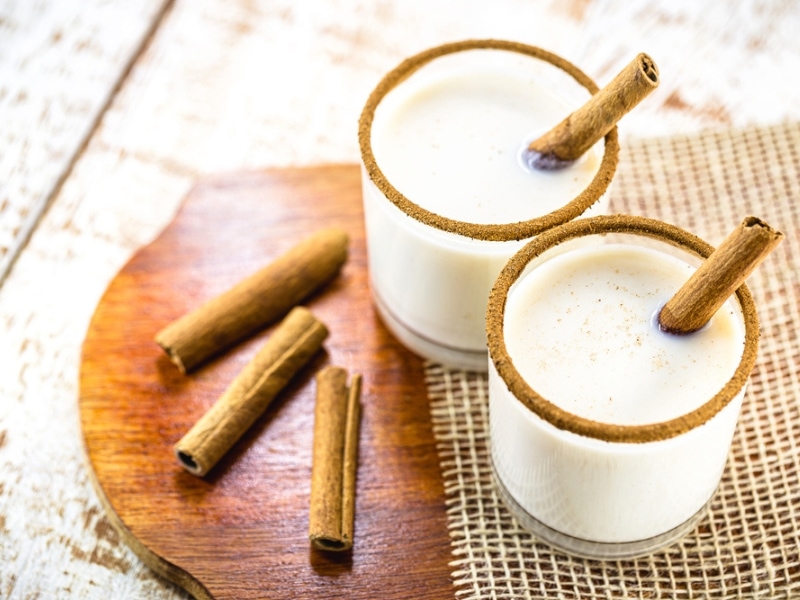Two Glasses of Homemade Eggnog Garnished with Powdered and Whole Cinnamon Sticks