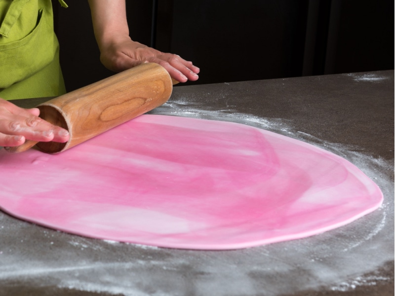 Woman Rolling Out Pink Fondant Icing Using a Wooden Pin