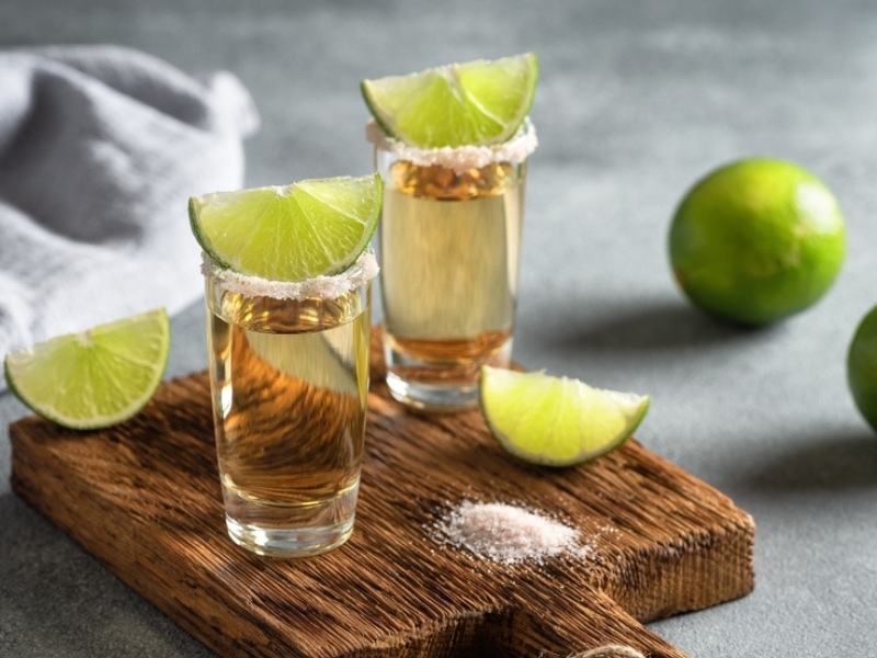 Joven Tequila dalam Gelas Tembakan Dengan Kapur dan Garam Merah Muda di Papan Kayu