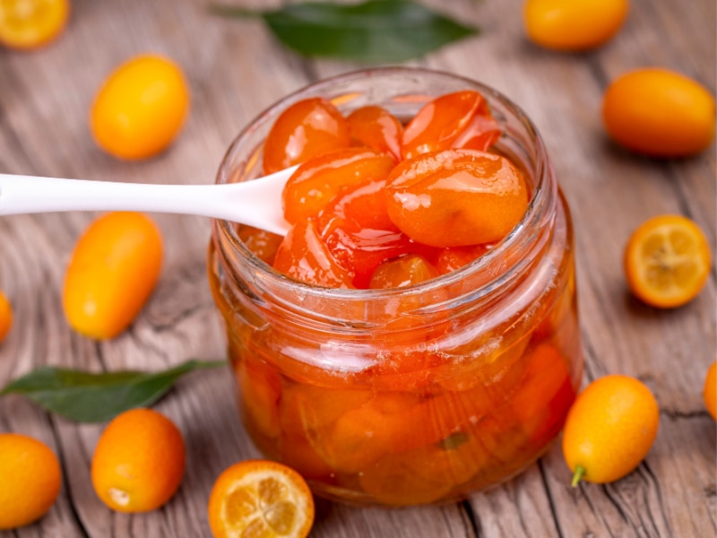 A Jar of Kumquat Jam and fresh kumquats on wooden table