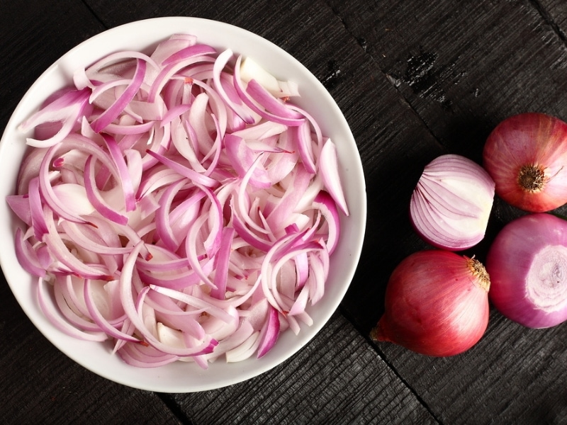 Peeled and Bowl of Sliced Red Onions on a Wooden Table
