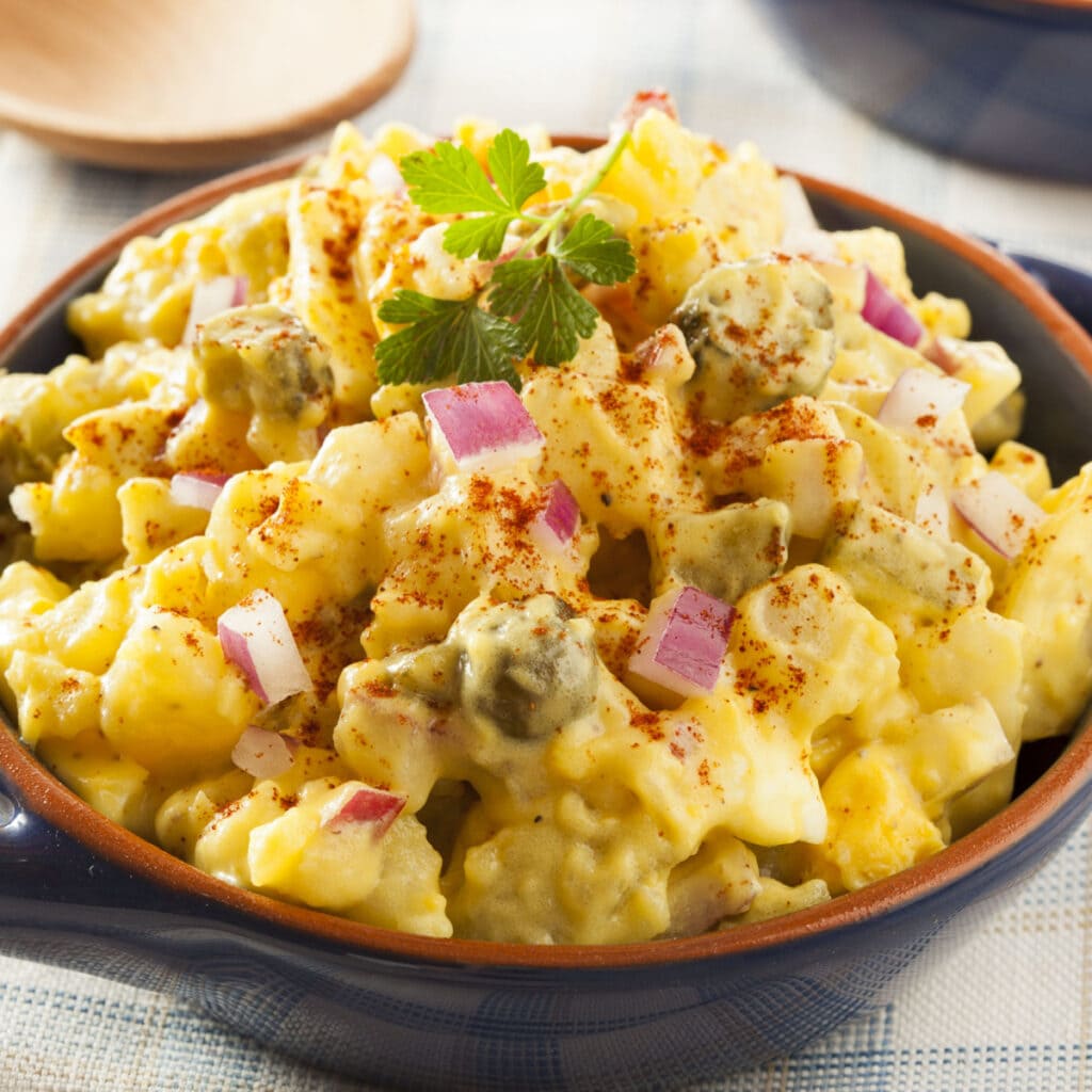 Creamy Potato Salad With Onion, Pickles and Eggs Garnished With Fresh Celery Leaves