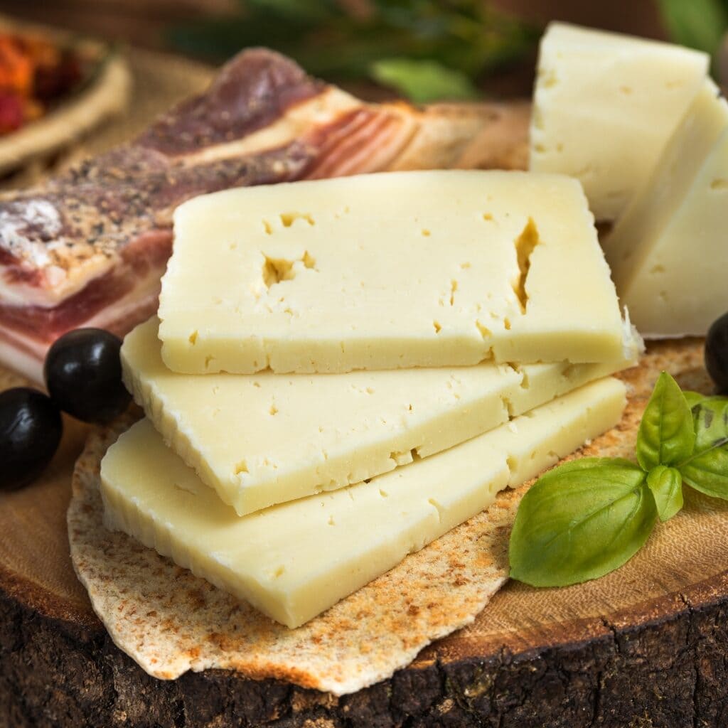 What Is Pecorino Cheese? -Everything You Need to Know featuring Sliced Italian Cheese Pecorino on a Wood Cutting Board with Prosciutto, Olives, And Basil