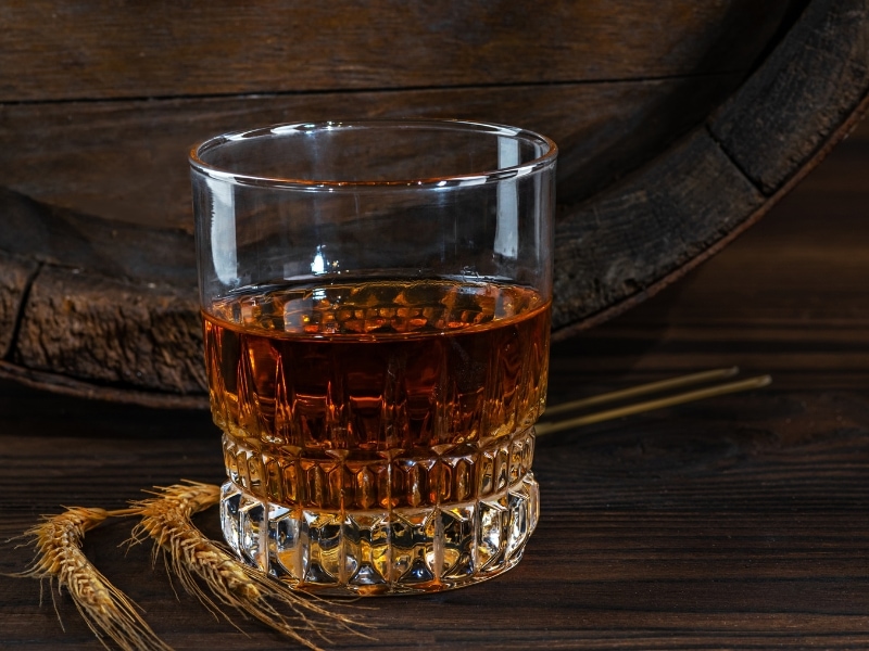 Glass of Wheat Whisky in Front of an Old Alcohol Barrel