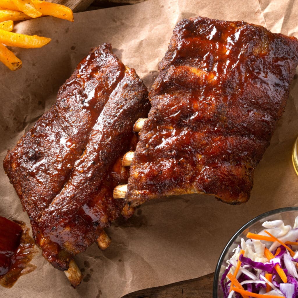 Savory Oven Baked Baby Back Ribs on a Parchment Paper with French Fries and Cole Slaw on the Sides      