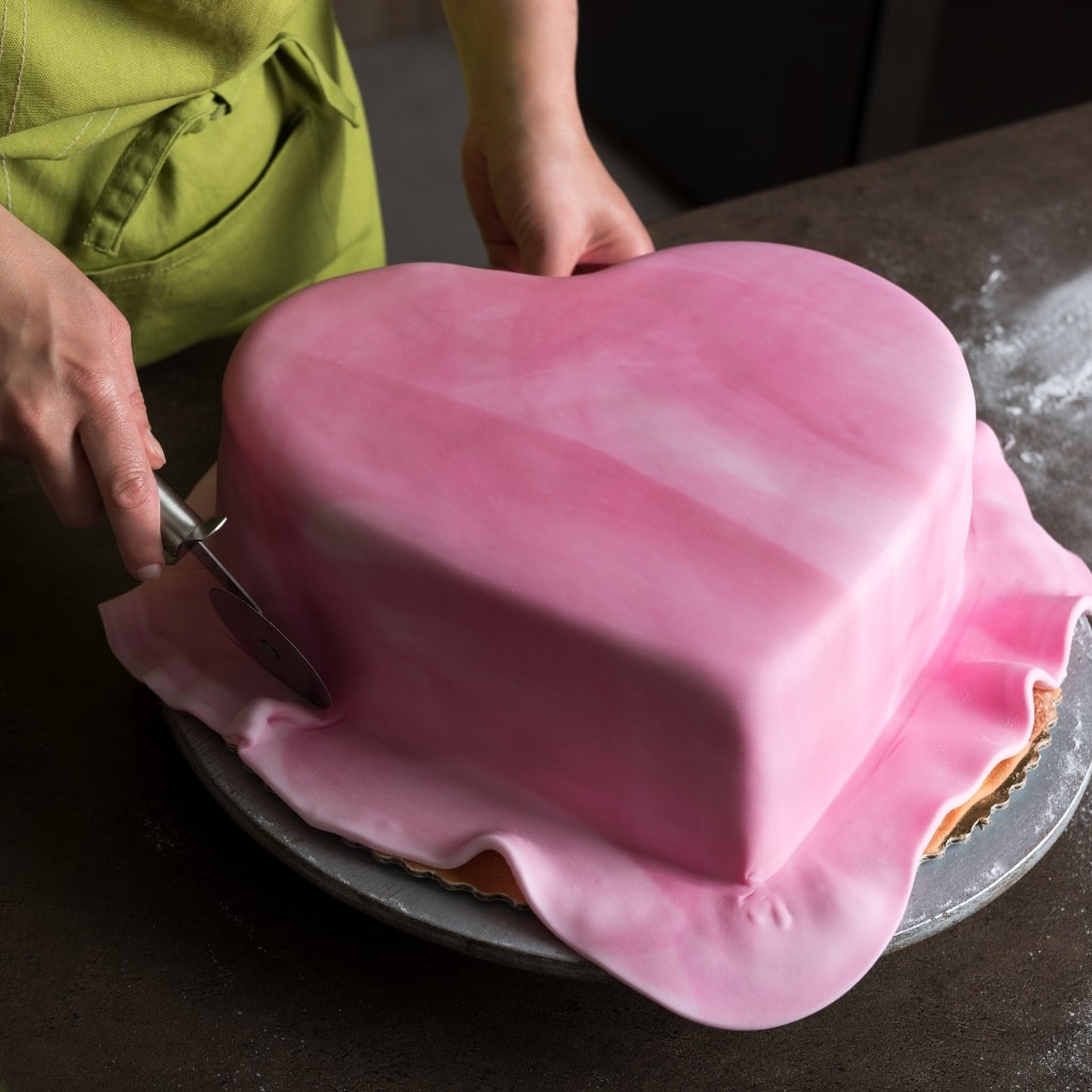 What Is Fondant Icing? (And How to Make It) featuring Woman Covering Heart-Shaped Cake in Marbled Pink Fondant