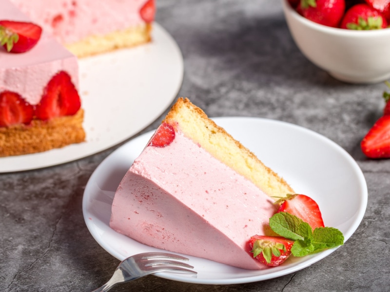 A Slice of Strawberry Cheesecake on a White Plate with Fresh Strawberries and a Silver Fork