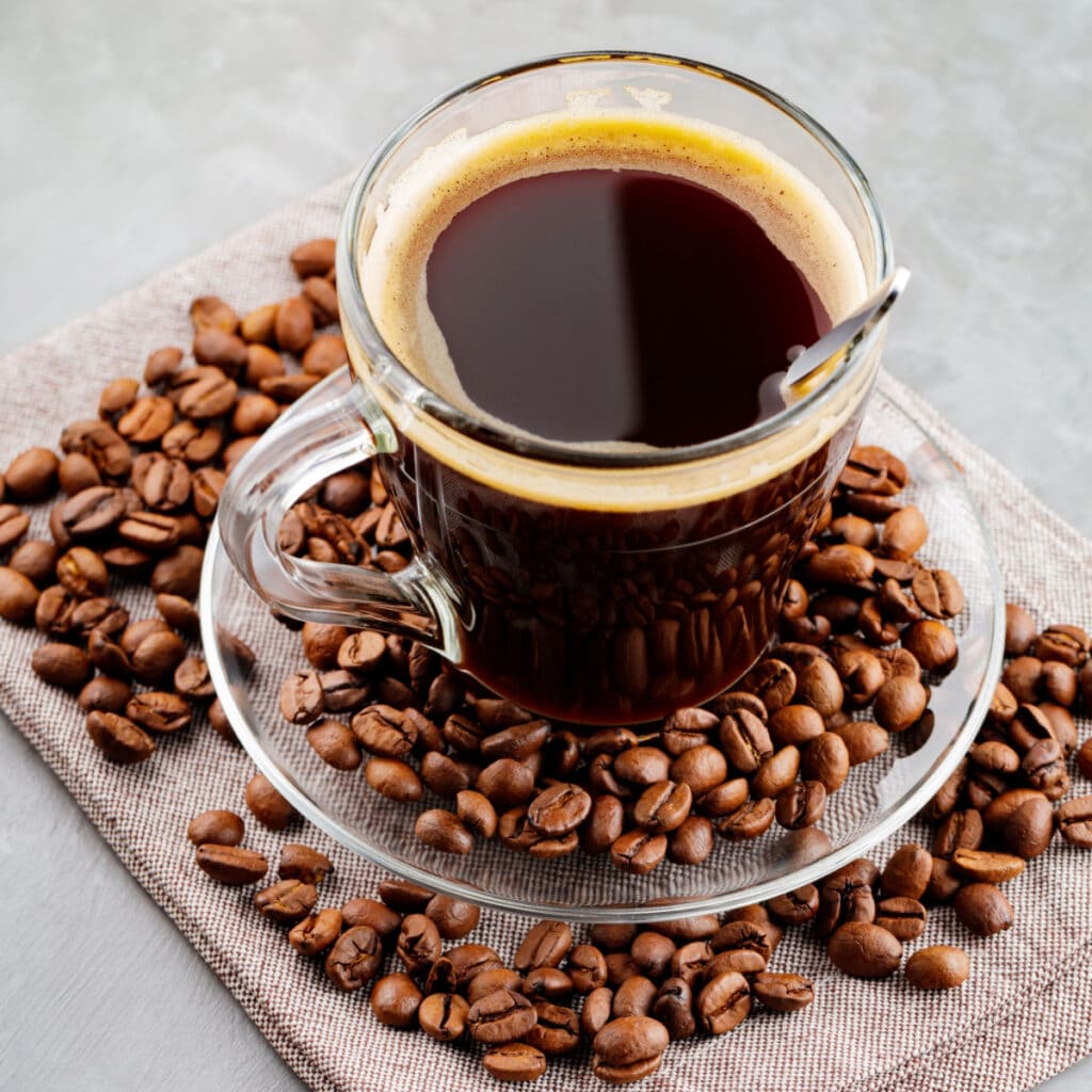 Americano Coffee in a Clear Glass Cup with Coffee Beans on Background 