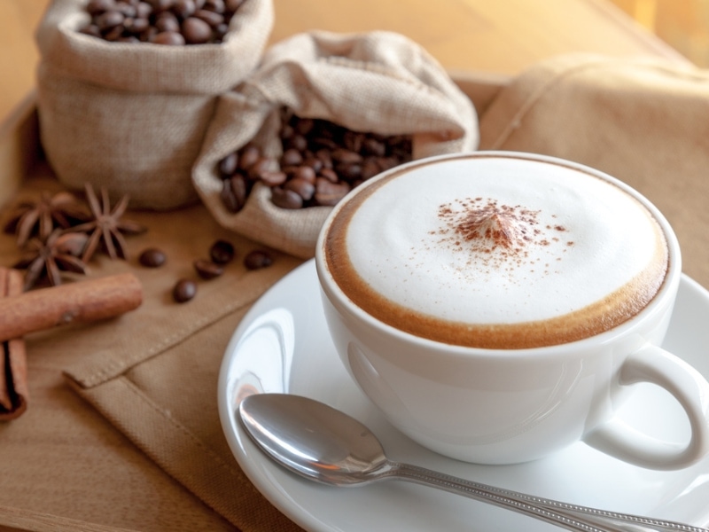 Cappuccino Busa dan Krim dalam Cangkir Kopi, Dengan Karung Biji Kopi dan Rempah-rempah di Latar Belakang